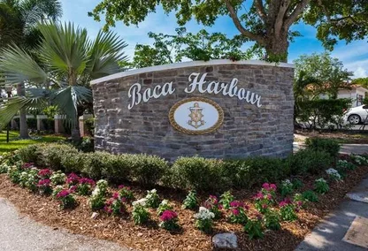Boca Harbour entrance sign in Boca Raton, featuring stonework, nautical emblem, and colorful landscaped flowers.